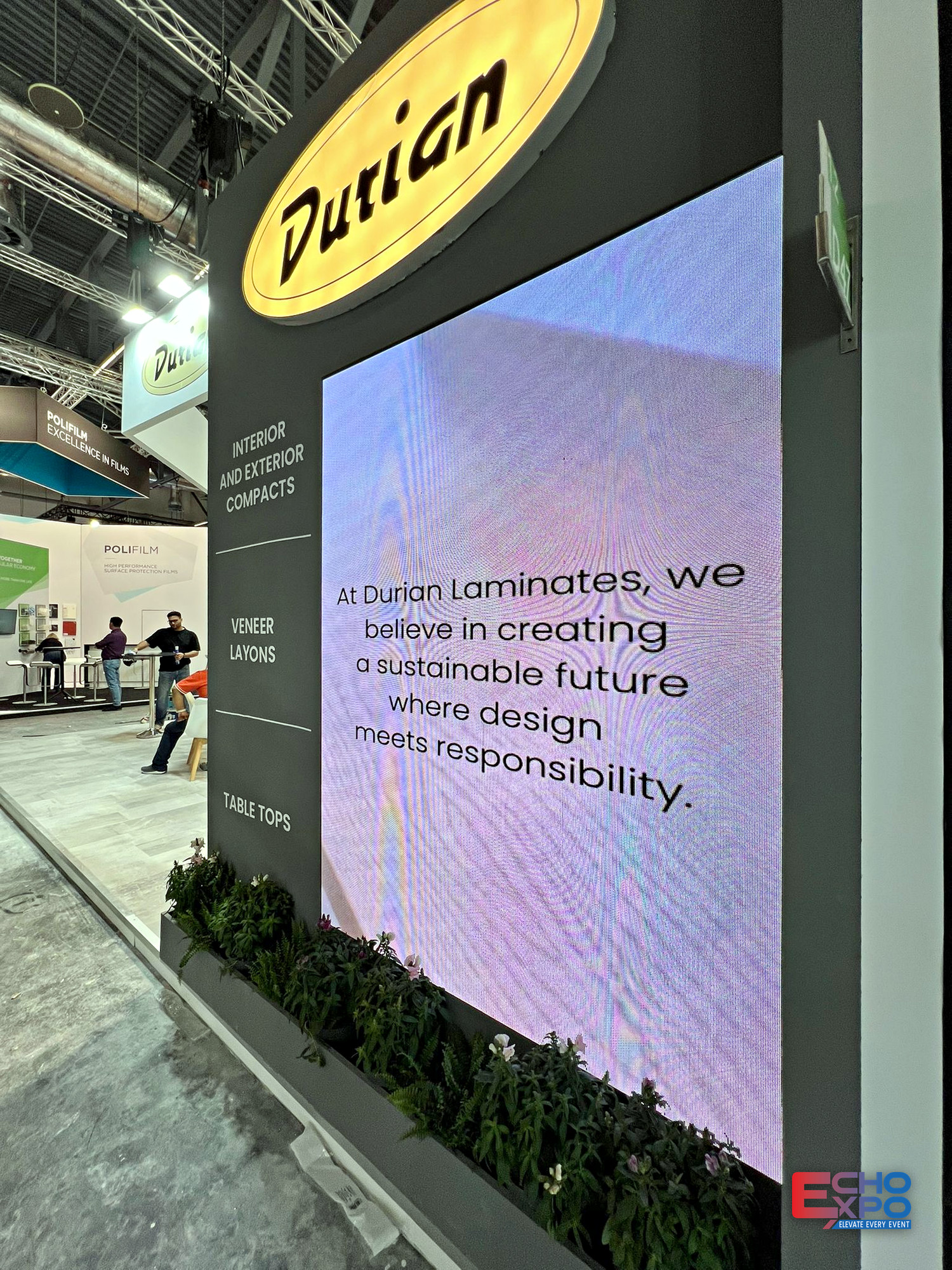 Durian Laminates stand at interzum Cologne 2025 seen along the aisle, with backlit product category panels and veneer sample displays.