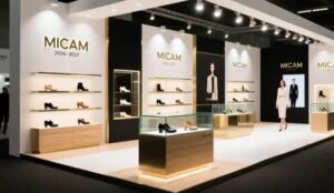 Footwear exhibition stand concept for MICAM Milano, with lit wall shelving, glass display cases and gold three-dimensional lettering