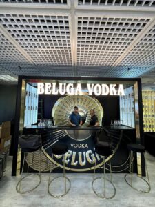 Beluga Noble Vodka bar stand at Bar Convent Berlin 2023, with an illuminated BELUGA VODKA sign, a gold sunburst bottle wall and gold bar stools in front of a black bar.