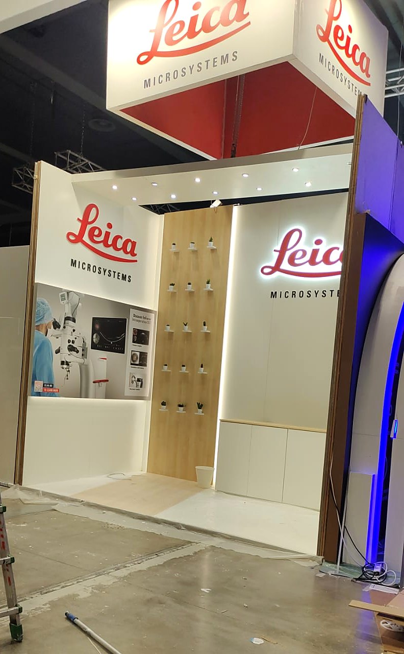 Leica Microsystems stand at ESCRS 2022 seen from the aisle, with a red and white hanging sign carrying the Leica logo above white walls and a timber feature panel.