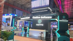UPGAMING exhibition stand at SiGMA Europe 2023 in Malta, with a hexagonal illuminated header, cyan LED pillars and a central black logo tower.
