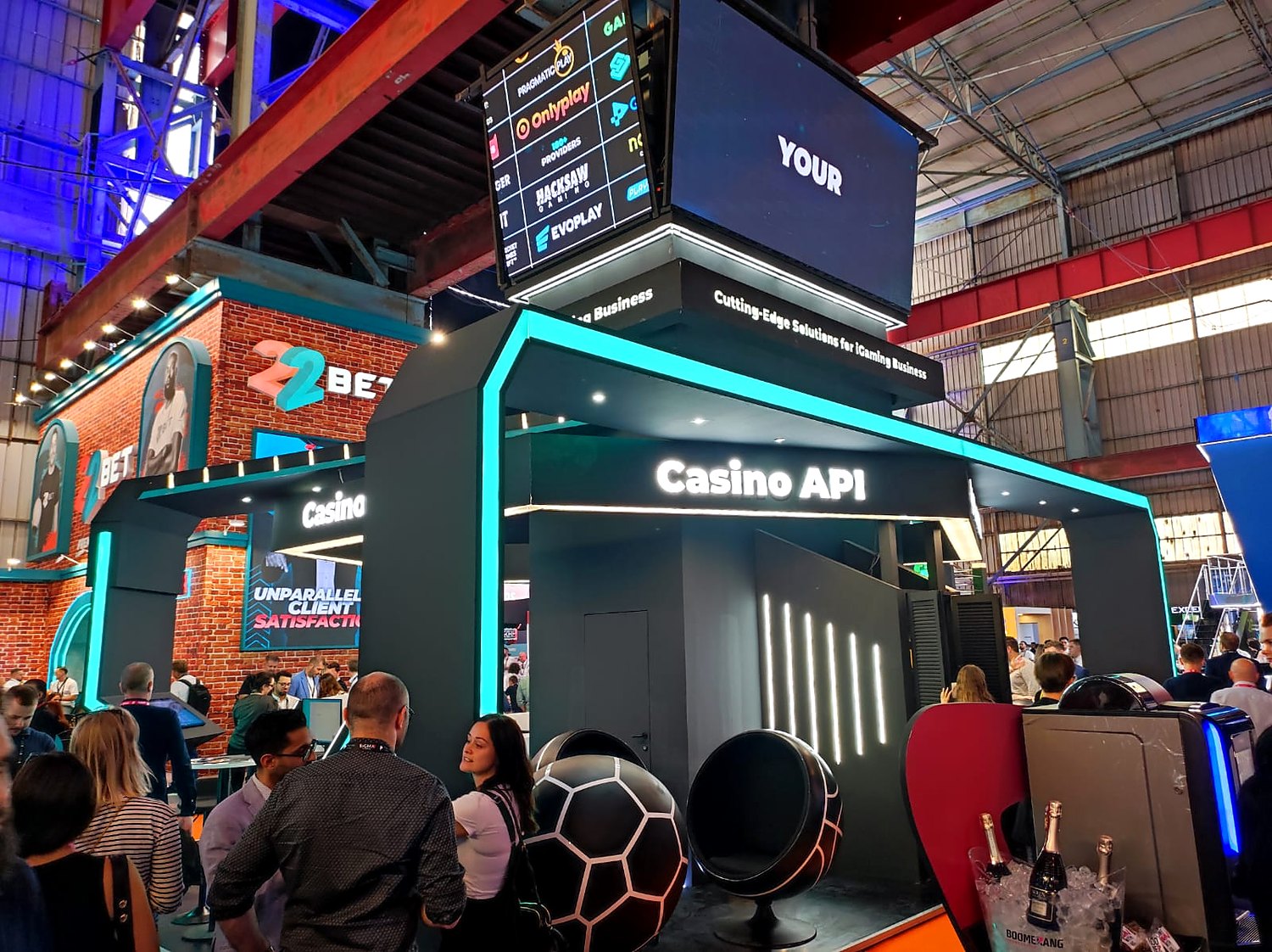 Visitors at the UPGAMING stand at SiGMA Europe 2023, gathered under the Casino Solution header beside football-styled egg chairs and a lit floor ring.