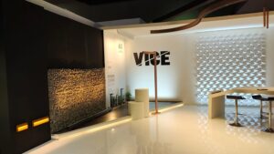 VICE lighting exhibition stand at Light + Building 2022 in Frankfurt: white gloss floor, a backlit perforated wall, a warm-lit stone gabion wall and the VICE logo in black.