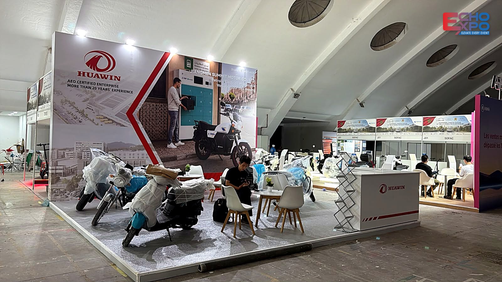 HUAWIN stand H07–H08 the day after build-up at EVS Mobility Expo Morocco 2026: motorcycles arriving in protective wrap on the finished stand.
