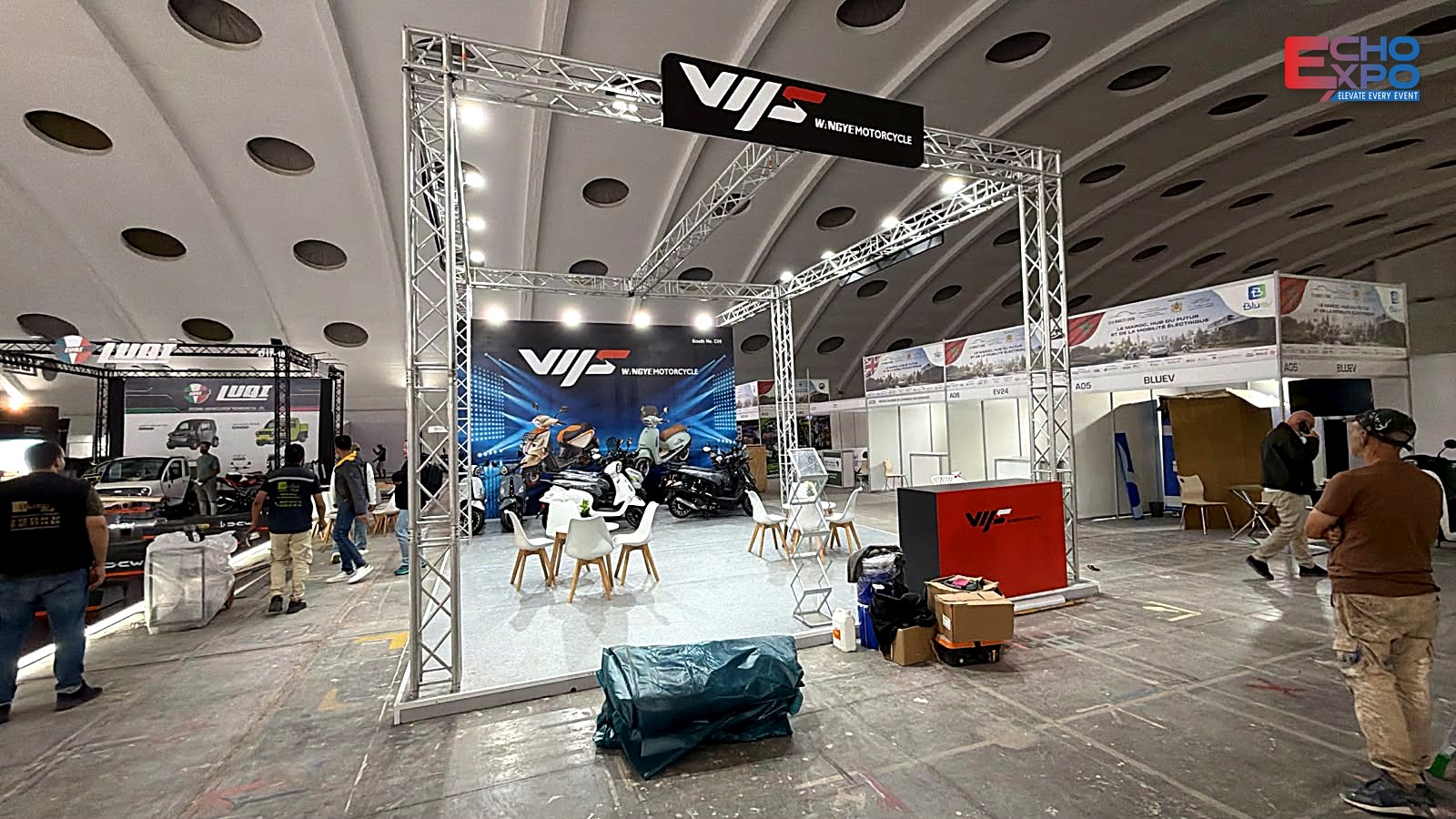 WANGYE Motorcycle stand structure complete before the carpet is laid: truss portal, lit fascia and graphic back wall, EVS Mobility Expo Morocco 2026.