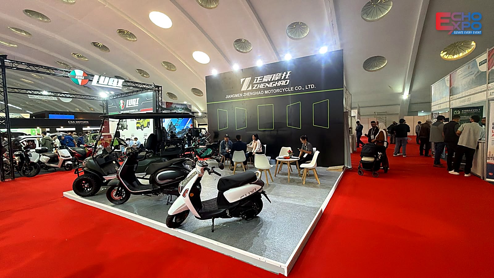 ZHENGHAO (Jiangmen Zhenghao Motorcycle) exhibition stand C17–C18 at EVS Mobility Expo Morocco 2026, OFEC Casablanca: black back wall with lime-green line graphics, lit from above, scooters and a utility vehicle on a raised grey floor.